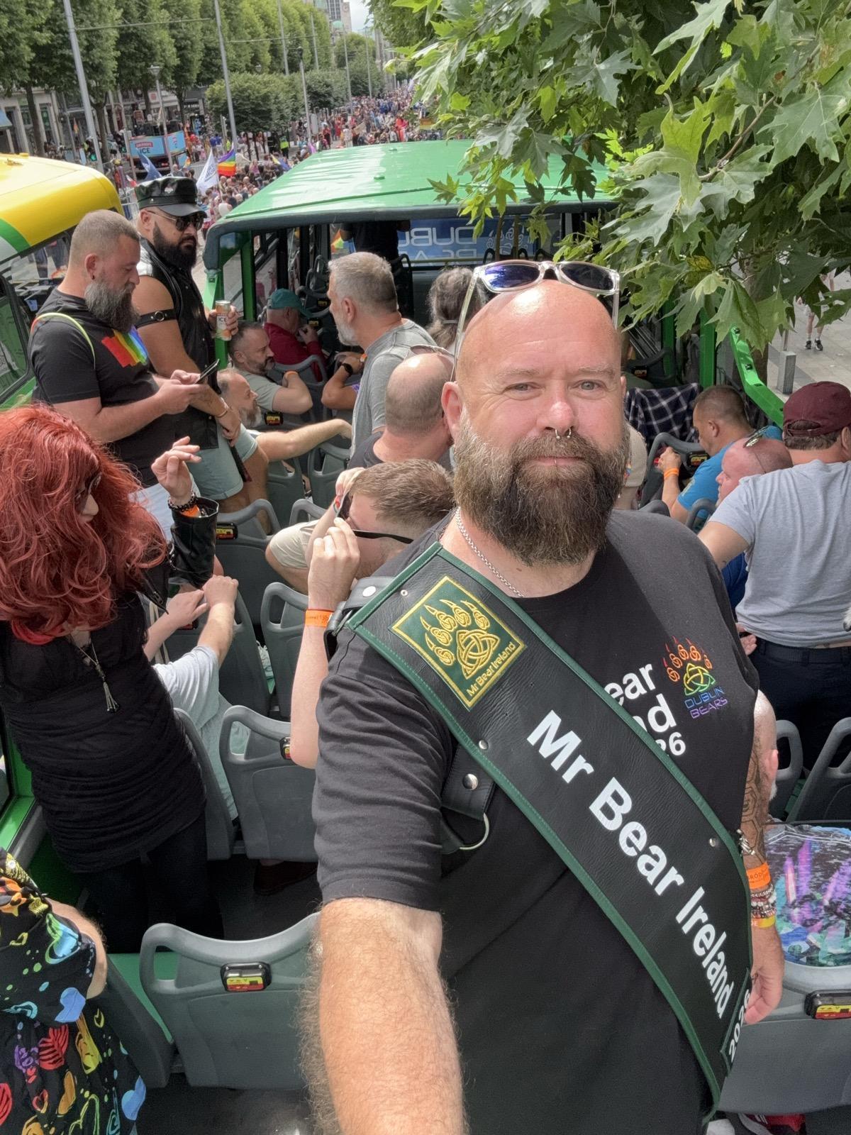 Rob on the bus with some bears and a drag queen in the background.